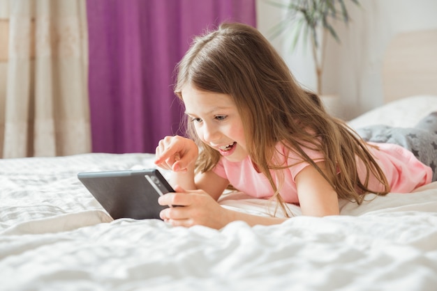 Gelukkig tiener meisje kijken naar online film met digitale mobiele tablet en liggend op bed thuis in de ochtend | Premium Foto