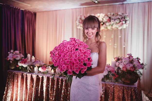 Gelukkige bruid met een groot boeket rozen. mooie jonge lachende bruid houdt grote bruiloft boeket met roze rozen. bruiloft in roze en groene tinten. de huwelijksceremonie. Premium Foto