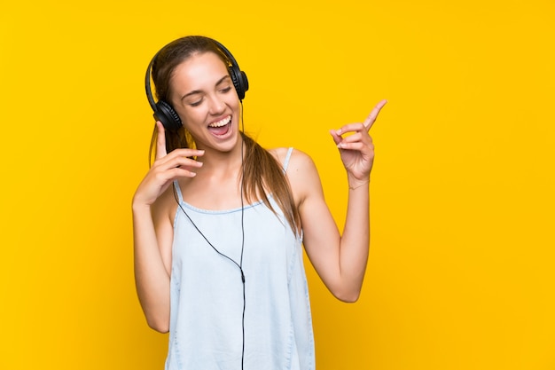 Gelukkige jonge vrouw het luisteren muziek over het geïsoleerde gele muur zingen Premium Foto