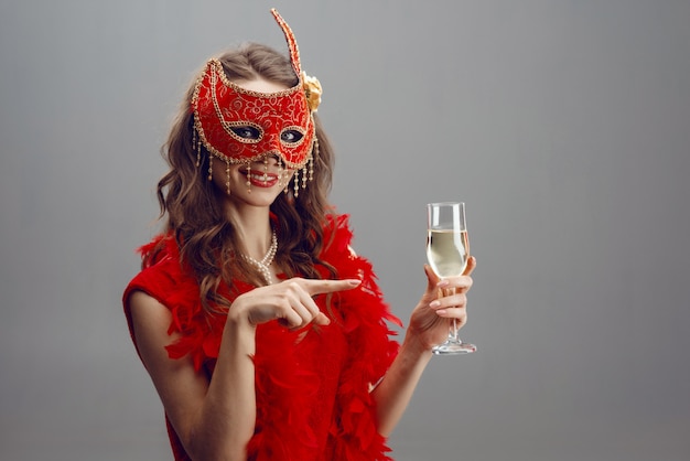 Gelukkige vrouw in een rood carnaval-masker en een boa met een opgeheven glas champagne Premium Foto