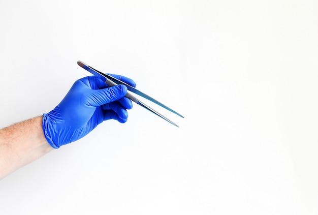Geneeskunde en chirurgiethema: de arts dient een blauw pincet van de handschoenholding in op wit wordt geïsoleerd dat Premium Foto
