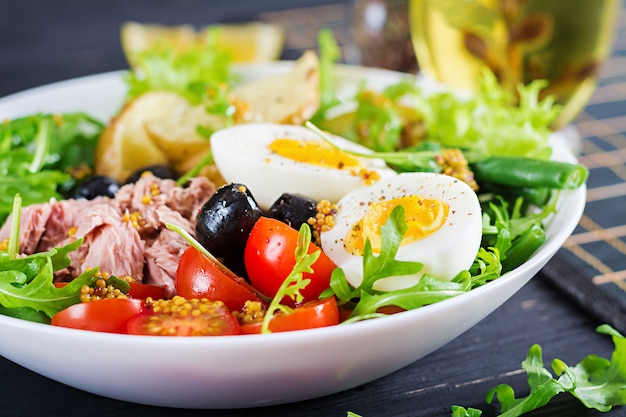 Gezonde stevige salade van tonijn, sperziebonen, tomaten, eieren, aardappelen, zwarte olijven close-up in een kom op tafel Gratis Foto