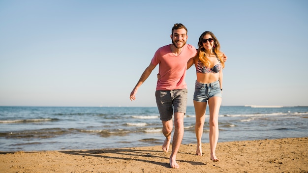 Glimlachend jong paar die samen op strand lopen Gratis Foto