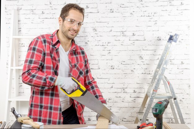 Glimlachende jonge mens die een raad met een handzaag snijdt Premium Foto