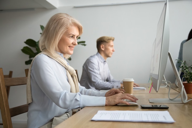 Glimlachende verouderde onderneemster die computer met behulp van die online in coworking bureau werkt Gratis Foto