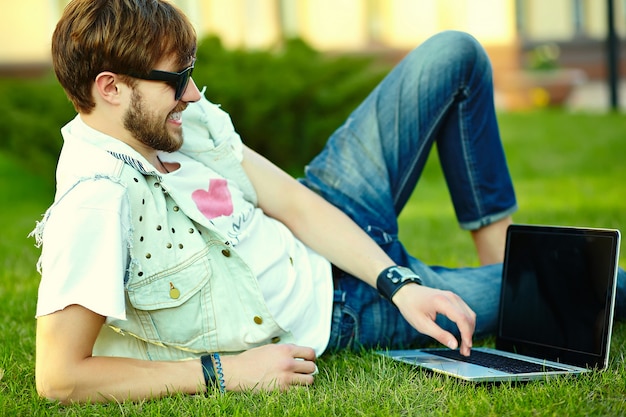 Grappige glimlachende hipster knappe mensenkerel in modieuze de zomerdoek in gras met notitieboekje Gratis Foto