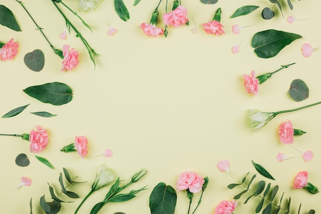 Groene eucalyptus populus bladeren; roze anjers en eustoma bloemen met ruimte in het midden op gele achtergrond Gratis Foto