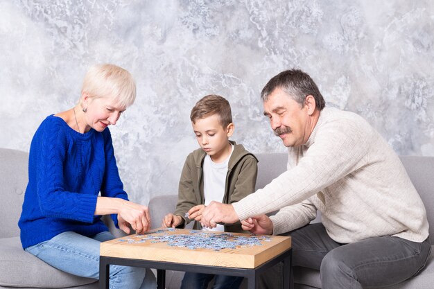 Grootmoeder, grootvader en kleinzoon verzamelen puzzels aan de tafel in de woonkamer. de familie brengt samen tijd door met het spelen van educatieve spelletjes Premium Foto