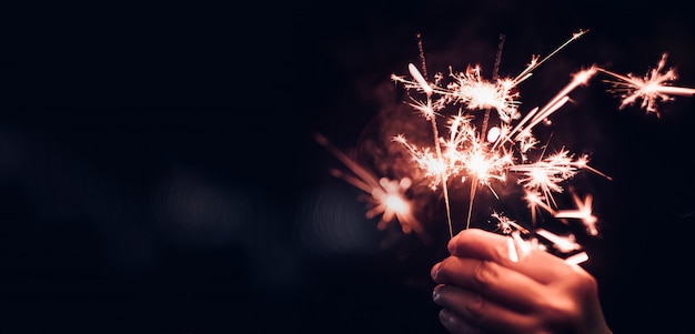 Hand met brandende sparkler ontploffing op een zwarte bokeh Premium Foto