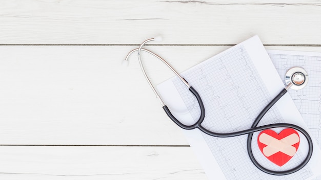 Hartvorm met verbanden en stethoscoop op ecg analyserrapport over houten lijst Gratis Foto