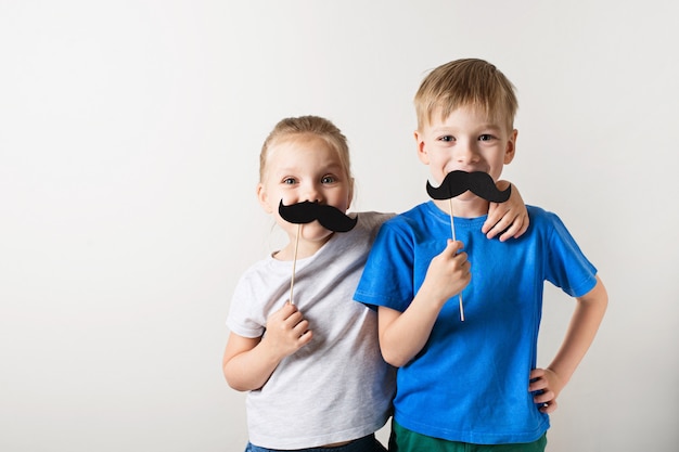 Het concept van de vadersdag, twee kleine kaukasische jonge geitjes die met snor op witte achtergrond glimlachen Premium Foto