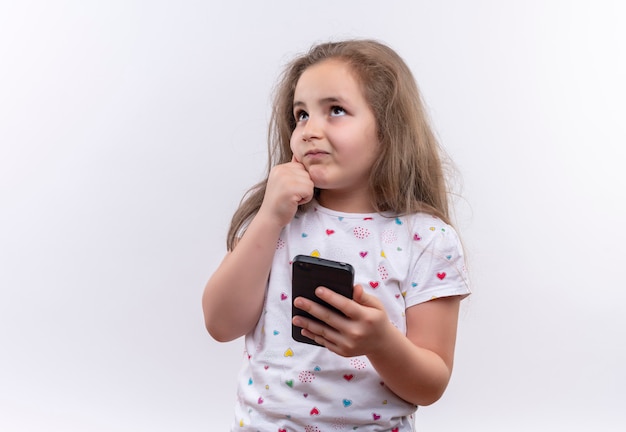 Sterkte Mededogen vandaag Het denkende kleine schoolmeisje die wit t-shirt dragen die telefoon houden  legde haar hand op de wang op geïsoleerde witte muur | Gratis Foto