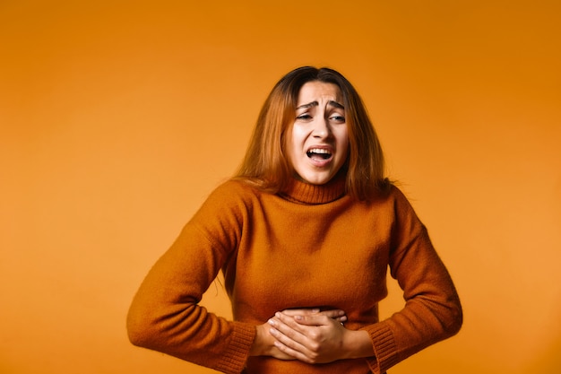 Het jonge meisje houdt voor haar maag en voelt pijn staand Gratis Foto