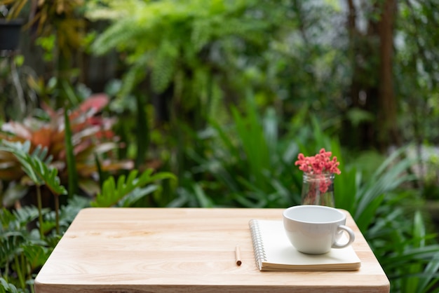 Het notitieboekje van de koffiekop, bruin potlood en mooie rode droge bloem in glasvaas op houten lijst Premium Foto