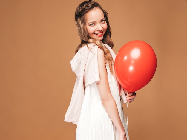 Het opgewekte jonge meisje stellen in trendy de zomer witte kleding. vrouwenmodel met het rode ballon stellen. klaar om te feesten Gratis Foto