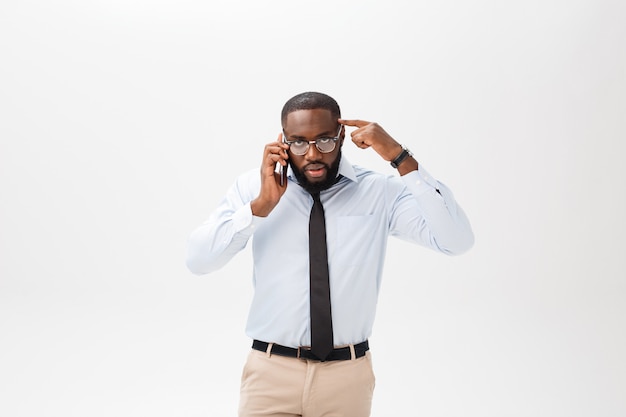 Het portret van een verwarde jonge afrikaanse mens kleedde zich in wit overhemd spreken op mobiele telefoon en gesturing geïsoleerd over witte achtergrond Premium Foto
