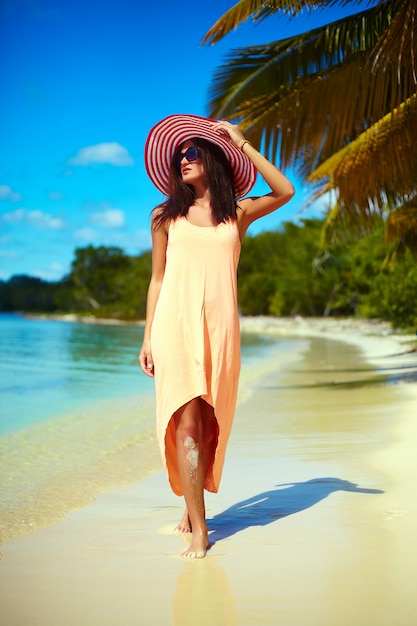 Hete mooie vrouw in kleurrijke sunhat en kleding die dichtbij strandoceaan lopen op hete de zomerdag dichtbij palm Gratis Foto