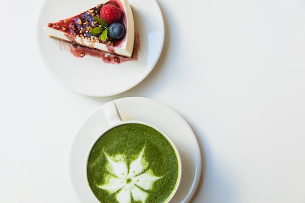 Japanse groene theematcha in witte kop en kaasbescake op plaat over witte achtergrond Gratis Foto