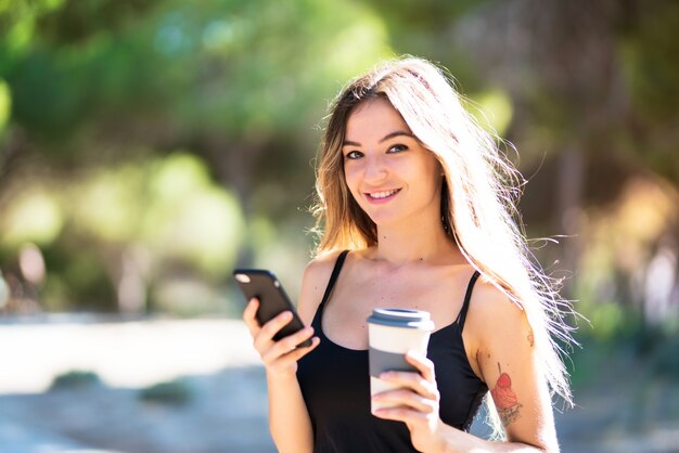 Jong meisje dat bij in openlucht koffie houdt om weg te nemen terwijl het verzenden van een bericht met mobiel Premium Foto