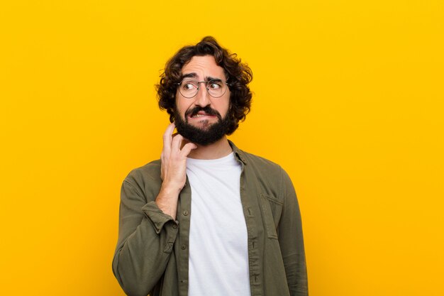 Jonge gekke man voelt zich gestrest, gefrustreerd en moe, wrijft pijnlijke nek, met een bezorgde, onrustige blik gele muur Premium Foto