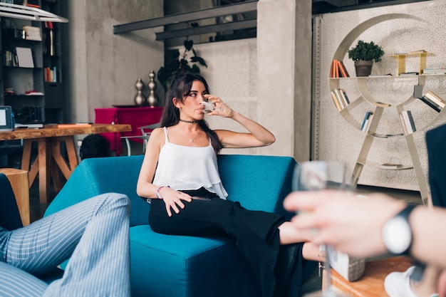 Jonge kaukasische vrouw die en met vrienden in moderne zolder drinkt zit Premium Foto