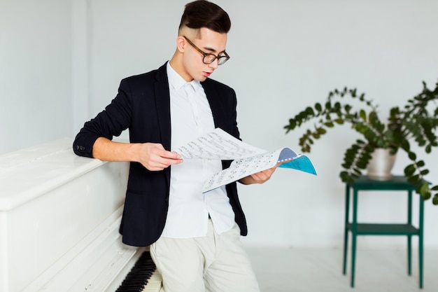 Jonge mens die zich dichtbij de piano bevindt die muzikaal blad bekijkt Gratis Foto