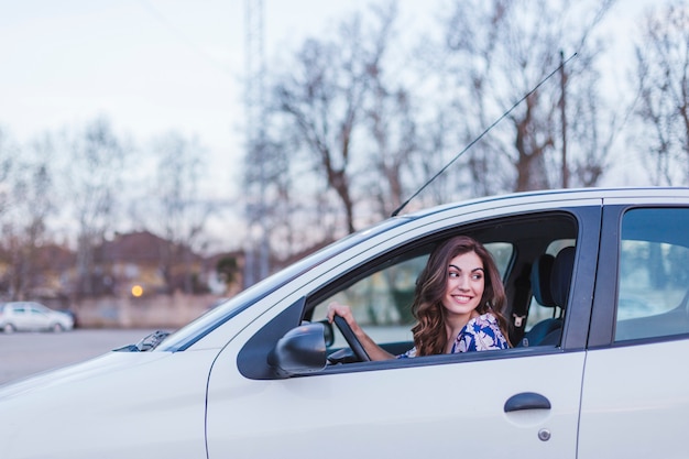 Jonge vrouw besturen van een auto in de stad. portret van een mooie vrouw in een auto, kijkt uit het raam en glimlacht. reizen en vakanties concepten Premium Foto