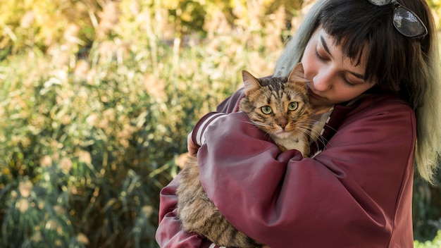 Jonge vrouw die haar gestreepte katkat in tuin koestert Gratis Foto