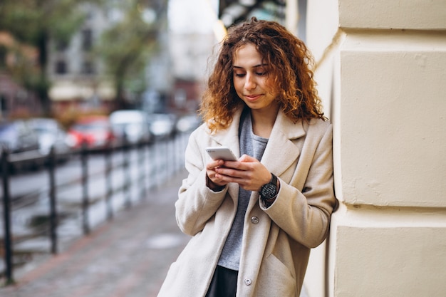 Jonge vrouw met krullend haar die telefoon met behulp van bij de straat Gratis Foto