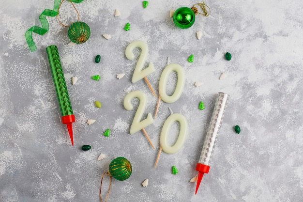 Kaarsen in de vorm van nummer 2020 als een symbool van het nieuwe jaar naast kerstvormig fonkelend snoep op een grijze tafel. bovenaanzicht, platliggend Gratis Foto
