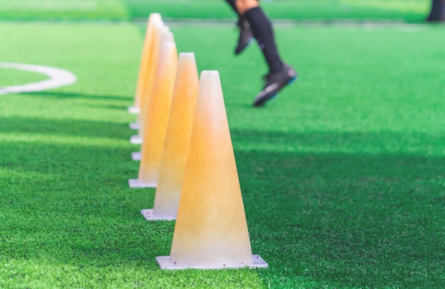 Kinderenvoeten met voetbalschoenen die op opleidingskegel op voetbalgrond opleiden Premium Foto