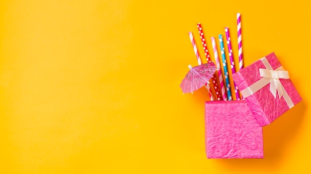 Kleurrijk het drinken stro met kleine paraplu in de roze doos op gele achtergrond Gratis Foto