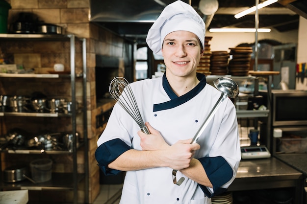 Koken staand met garde en pollepel in de keuken Gratis Foto