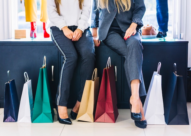 Lage gedeelte van twee vrouwelijke zitten in de winkel met kleurrijke boodschappentassen Gratis Foto