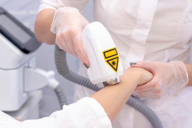 Laser ontharing en cosmetologie. het meisje verwijdert haar op haar arm met een laser. cosmetologie ontharingsprocedure. laser ontharing en cosmetologie. cosmetologie en spa concept Premium Foto