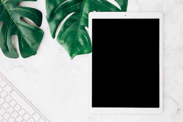 Leeg scherm digitale tablet met monstera bladeren en toetsenbord op witte marmeren bureau Gratis Foto