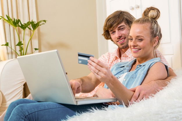Leuk paar die laptop met behulp van om online het winkelen zitting op de laag in de woonkamer te doen Premium Foto