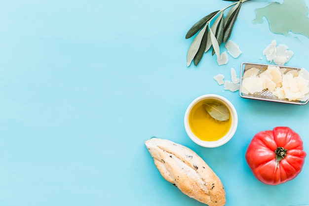 Luchtmening van brood, olie, geraspte kaas en tomaat op blauwe achtergrond Gratis Foto