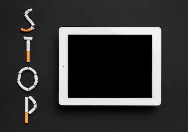 Luchtmening van digitale die tablet met eindewoord van sigaret tegen zwarte achtergrond wordt gemaakt Gratis Foto