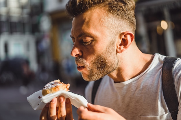 Man die nederlandse wafels in de straat dichtbij koffie eet. straatvoedsel in holland. Gratis Foto