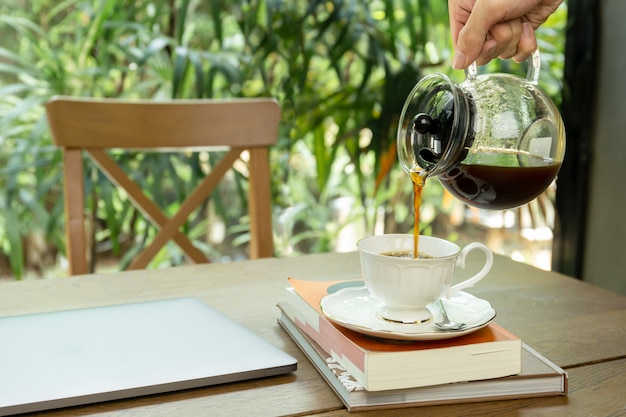 Man koffie gieten in een beker met laptop op de tafel. Premium Foto