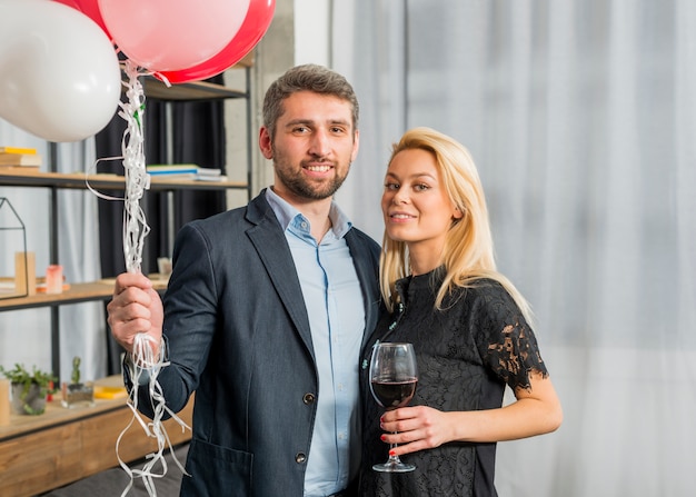 Man met ballonnen in de buurt van vrouw met een glas wijn in de kamer Gratis Foto
