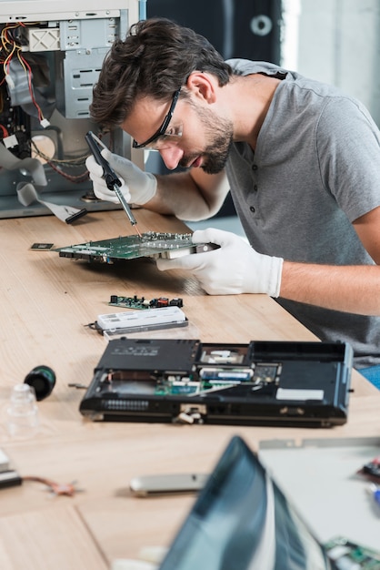 Mannelijke technicus die computermotherboard herstelt op houten bureau Gratis Foto