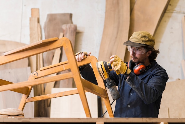 Mannelijke timmerman die een hout met orbitale schuurmachine in een workshop schuren Gratis Foto