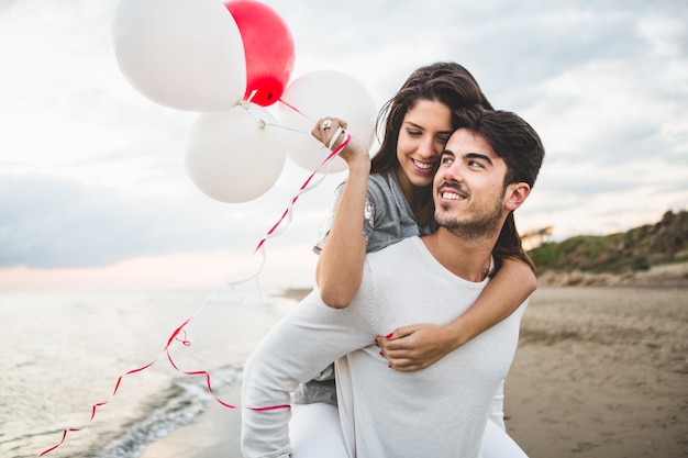 Meisje lacht met ballonnen, terwijl haar vriendje haar draagt op haar rug Gratis Foto