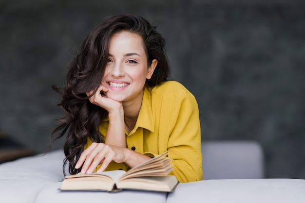 Middellange geschotene vrouw die met boek bij camera glimlachen Gratis Foto