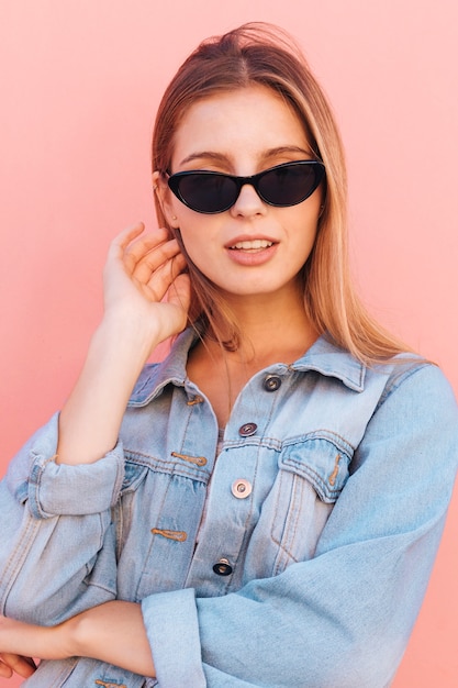 Modieuze jonge vrouw in blauw denimoverhemd die zich tegen roze achtergrond bevinden Gratis Foto