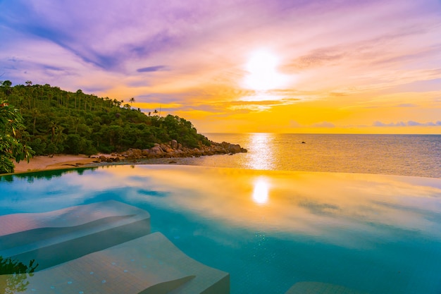 Mooi openlucht oneindigheids zwembad met kokosnotenpalm rond strand overzeese oceaan in zonsopgang of zonsondergangtijd Gratis Foto