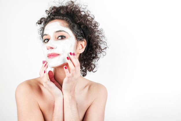 Mooie jonge vrouw wat betreft haar gezichtsmasker dat op witte achtergrond wordt geïsoleerd Gratis Foto