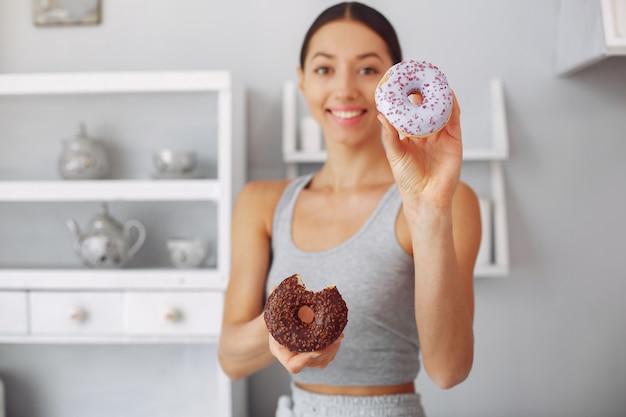 Mooie vrouw die zich in een keuken met doughnut bevindt Gratis Foto